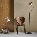 Blux T30 Aluminium Dome Table Lamp in white on a stack of books, shown with a matching black-and-copper floor lamp beside a wooden chair.
