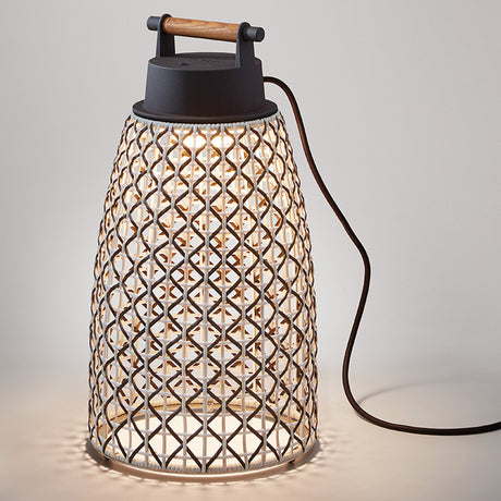 Nans Portable M/49 LED outdoor table lamp with tapered beige woven lattice shade, dark top, and wood carry handle, shown lit on a plain light grey background.