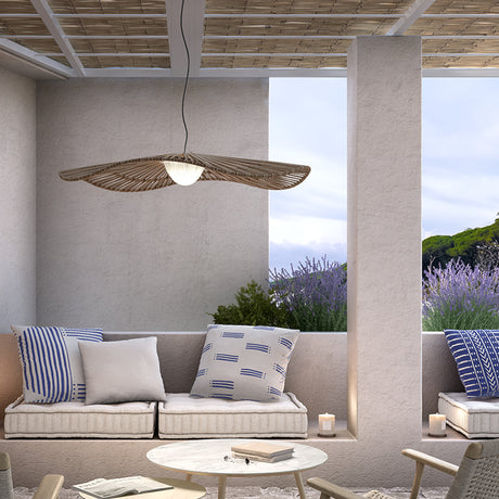 Mediterrània S/105 outdoor pendant light with wide disc-shaped brown slatted shade and white ribbed LED diffuser, hung above a coastal-style patio seating area.