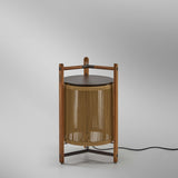 Kando P/76 outdoor floor lamp with sand nautical cord cylinder, three-legged teak wood frame, dark round lid, and wooden carry handle, shown on a plain light grey background.