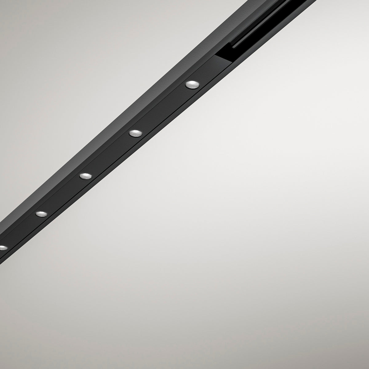 Close-up of the Street Spot Linear LED Track Spotlight in black, a slim diagonal profile with a row of round light openings and visible fixing screws on a plain light grey background.