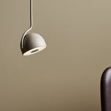Bowee S1 Dome LED Pendant Light in beige, with a single dome shade on a slim bent stem, shown against a neutral wall beside a dark upholstered chair.