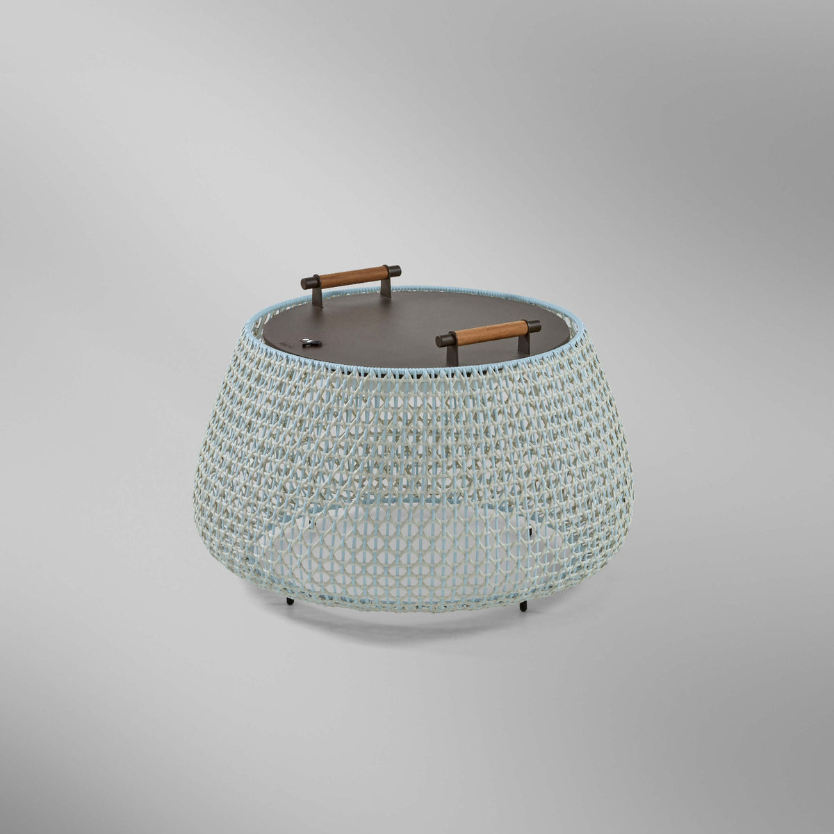 Nans Bag/38/R rechargeable outdoor floor lamp with a low, round woven basket body in beige with light blue and grey tones, dark round top and two carry handles, on a plain light background.