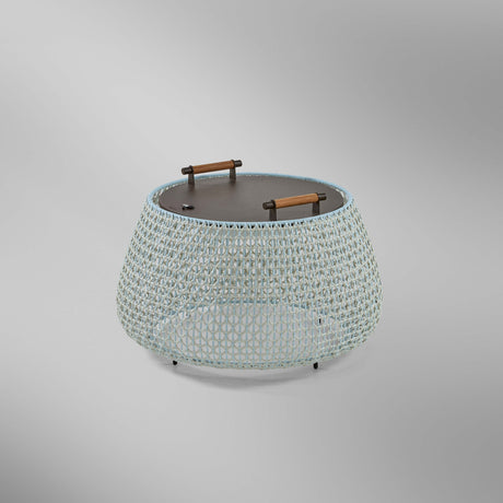 Nans Bag/38/R rechargeable outdoor floor lamp with a low, round woven basket body in beige with light blue and grey tones, dark round top and two carry handles, on a plain light background.