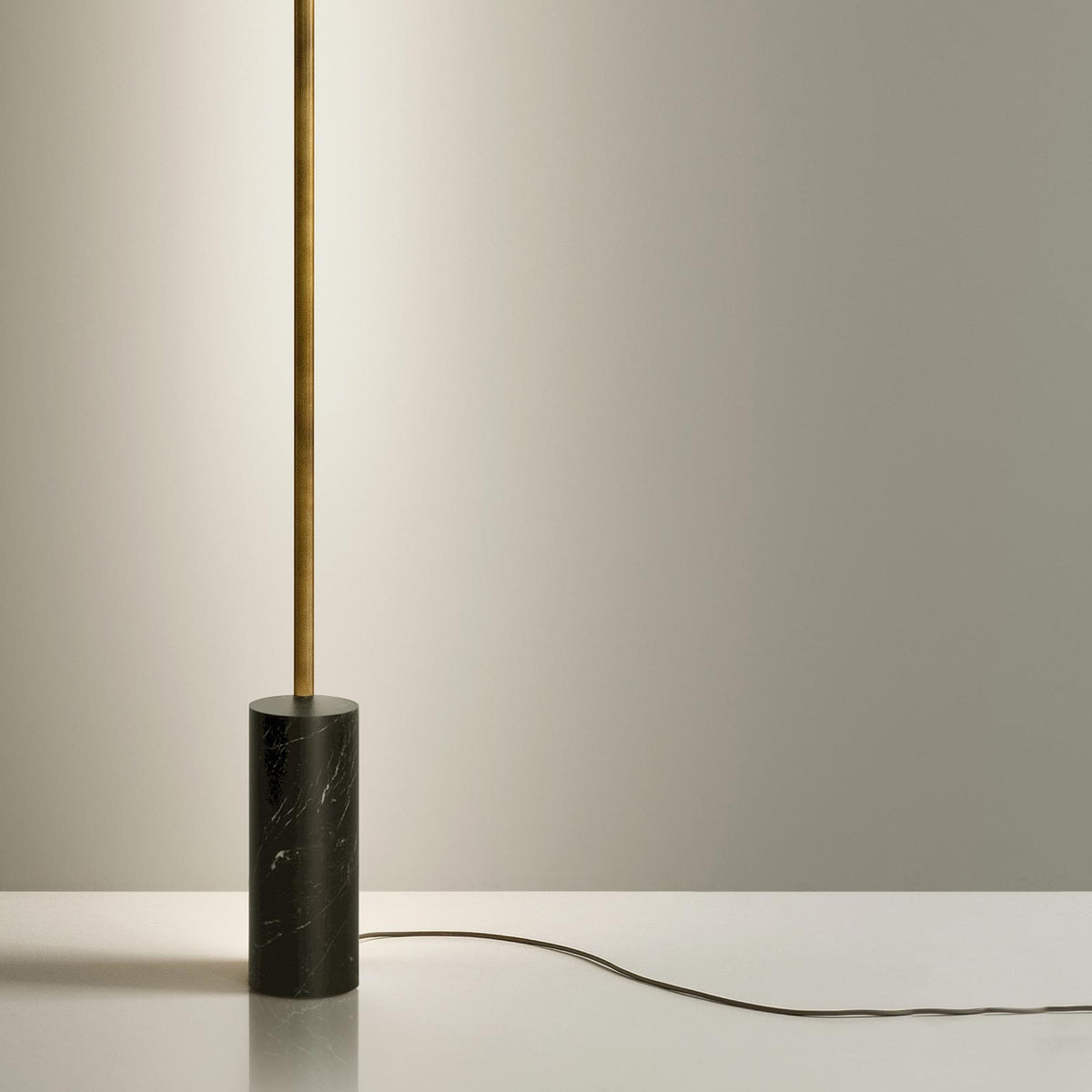 Hilow Line Nero Marquina linear floor lamp with slim brushed brass rod rising from a black, white-veined marble cylindrical base, shown against a neutral background.