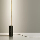 Hilow Line Nero Marquina linear floor lamp with slim brushed brass rod rising from a black, white-veined marble cylindrical base, shown against a neutral background.