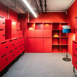 Aspen F40 Brass Drum Floor Lamp with white and blue stacked drum shade on a slim black stem and round base, shown in a red-themed room with cabinetry and shelving.