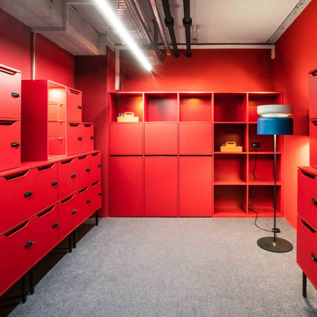 Aspen F40 Brass Drum Floor Lamp with white and blue stacked drum shade on a slim black stem and round base, shown in a red-themed room with cabinetry and shelving.