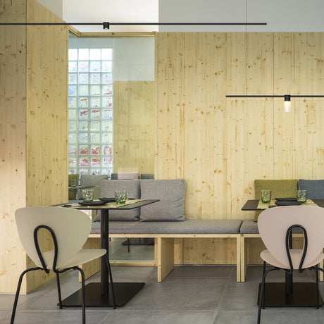SIS Spot Glass LED track spotlights in black on slim ceiling-mounted rails, lighting a wood-panelled dining area with grey bench seating and chairs.