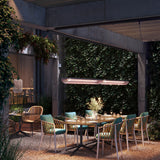 Nans Balis S/140 Outrack outdoor track pendant light with brown finish and openwork lattice shade, suspended above an outdoor dining table amid ivy-covered walls.