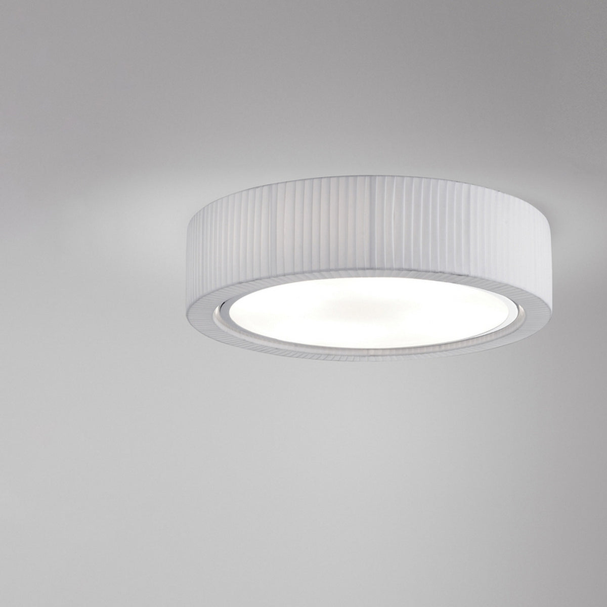 Urban PF/60 Ribbon LED ceiling light with a round drum shade in pleated white translucent ribbon, iron frame, and a broad white diffuser, shown against a plain grey background.