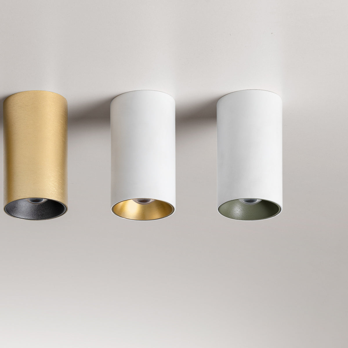Three 432 Ways Cylinder LED ceiling lights mounted in a row, surface-mounted cylinders in brushed gold, white with gold interior, and white with green interior finishes.