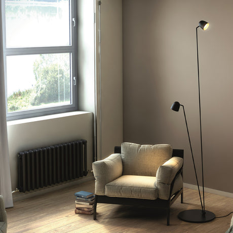 Speers F 2 Light LED Floor Lamp in matte black with two dome-shaped heads on slim stems and a round base, shown beside a beige armchair in a living room.
