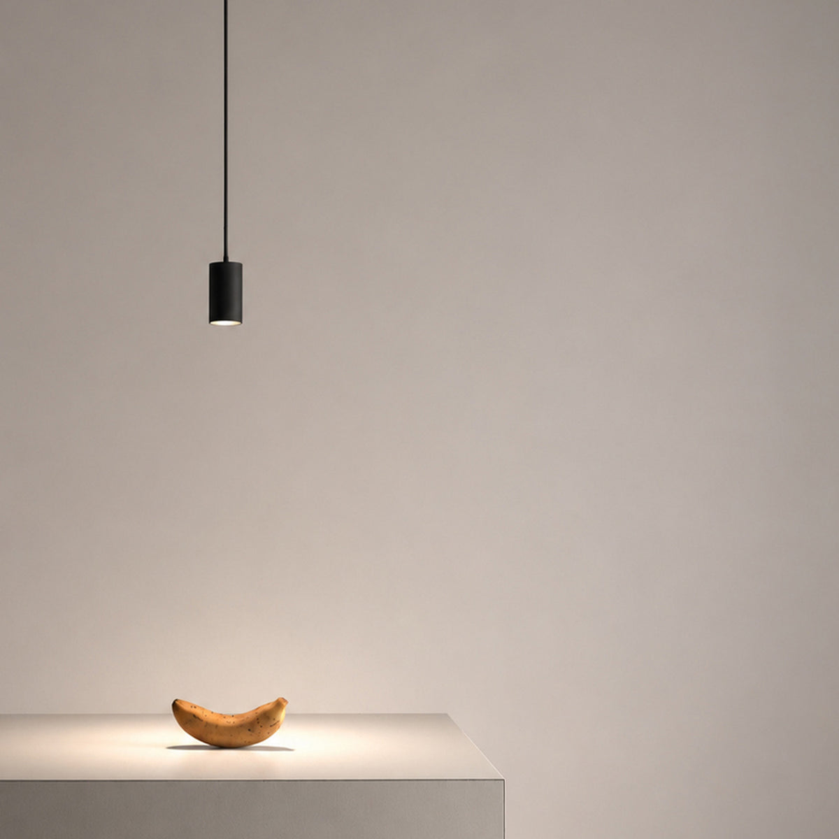 Anvil Spot SR 60° black cylindrical LED pendant light on a fine cord, casting a focused downlight onto a wooden sculpture on a plinth against a neutral background.
