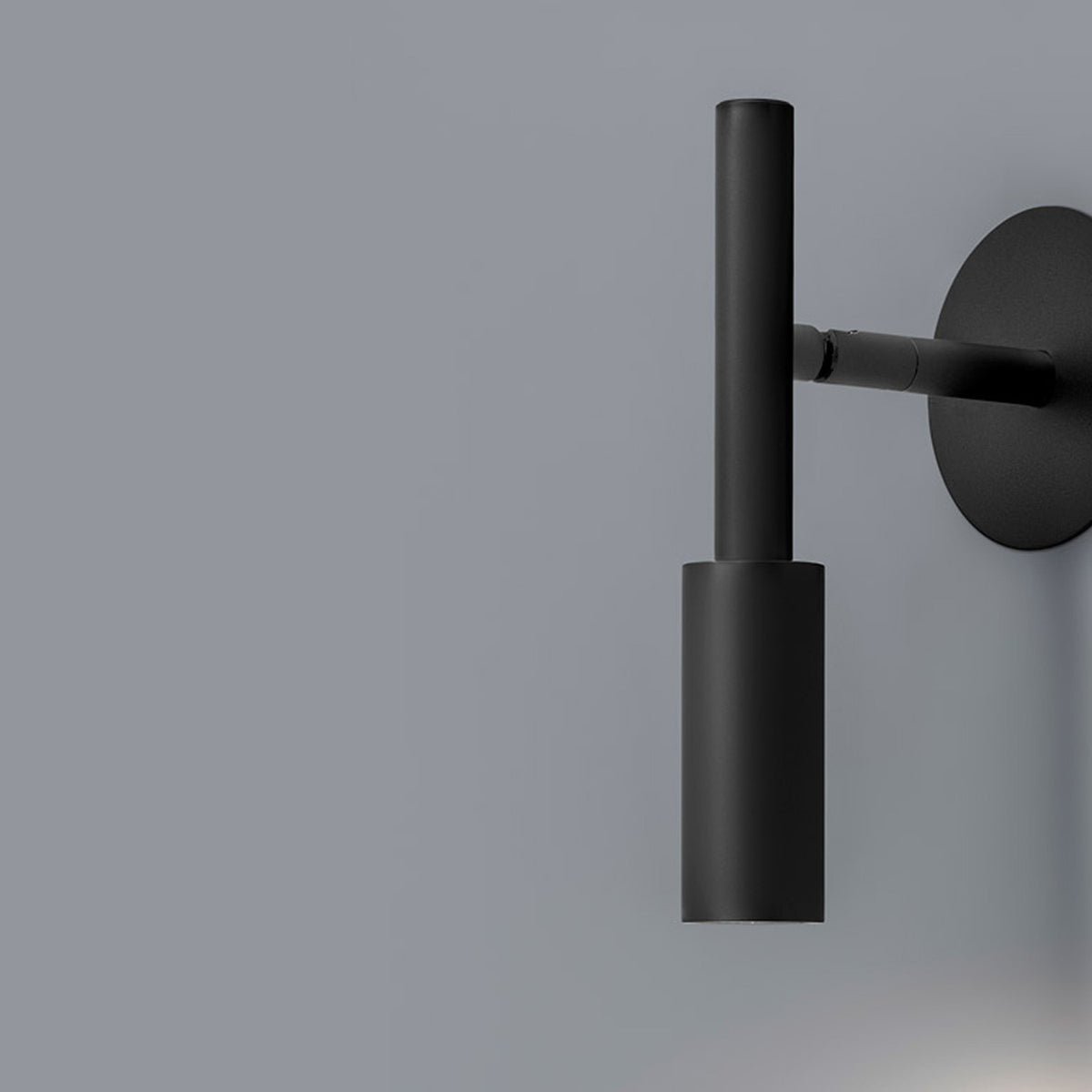 Tubino aluminium LED wall light in matt black, cylindrical head on a slim rod, mounted via a short arm from a round wall plate, shown against a grey background.