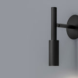 Tubino aluminium LED wall light in matt black, cylindrical head on a slim rod, mounted via a short arm from a round wall plate, shown against a grey background.