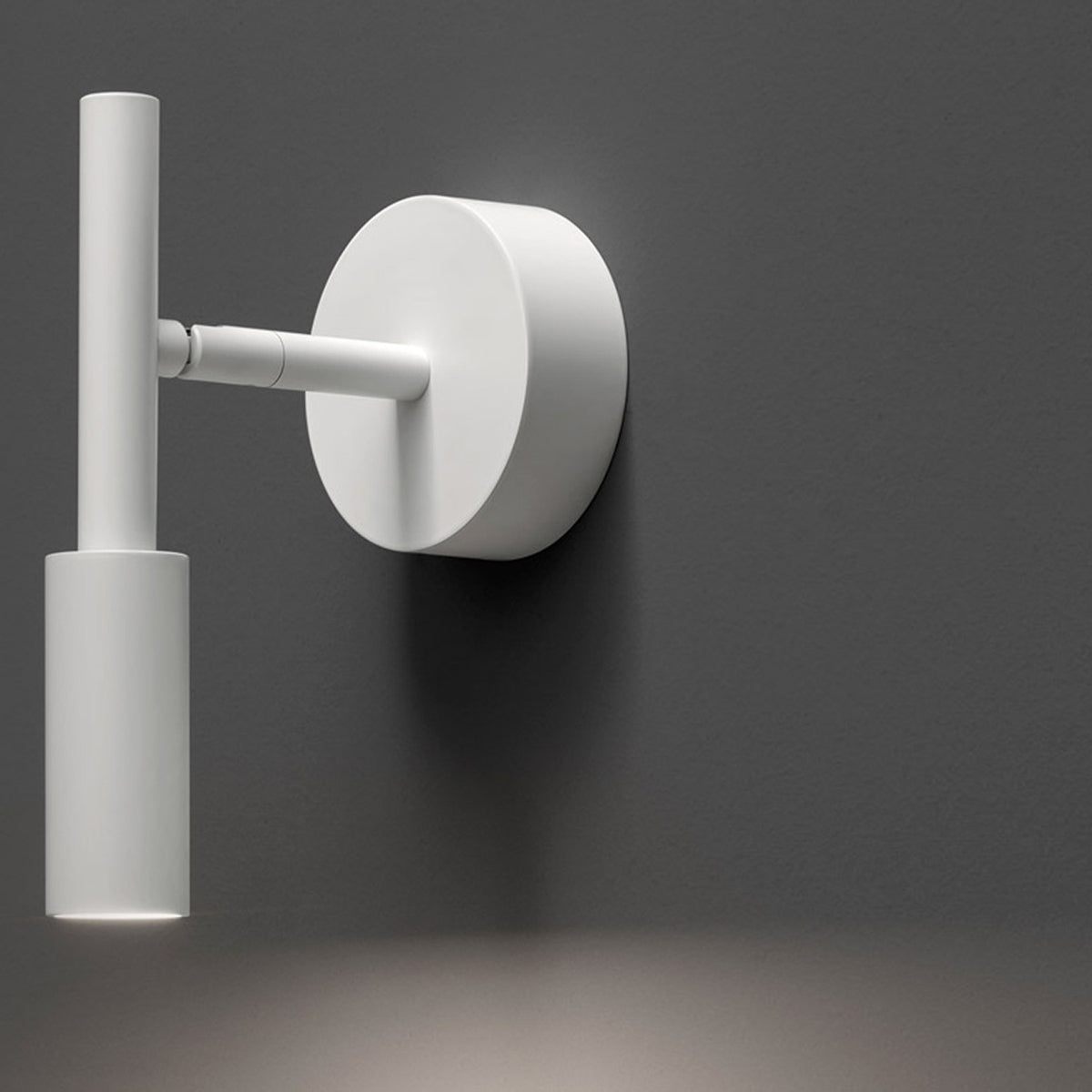 Tubino Aluminium LED Wall Light in white, a slim tube fixture on an adjustable arm from a round wall plate, shown against a dark grey background.