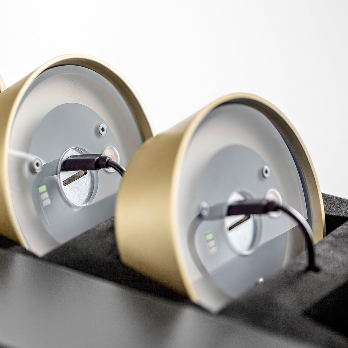 Close-up rear view of Firefly in the Sky rechargeable bollard lights in brushed champagne, showing round metal bases with charging ports and indicator lights, set against a plain background.