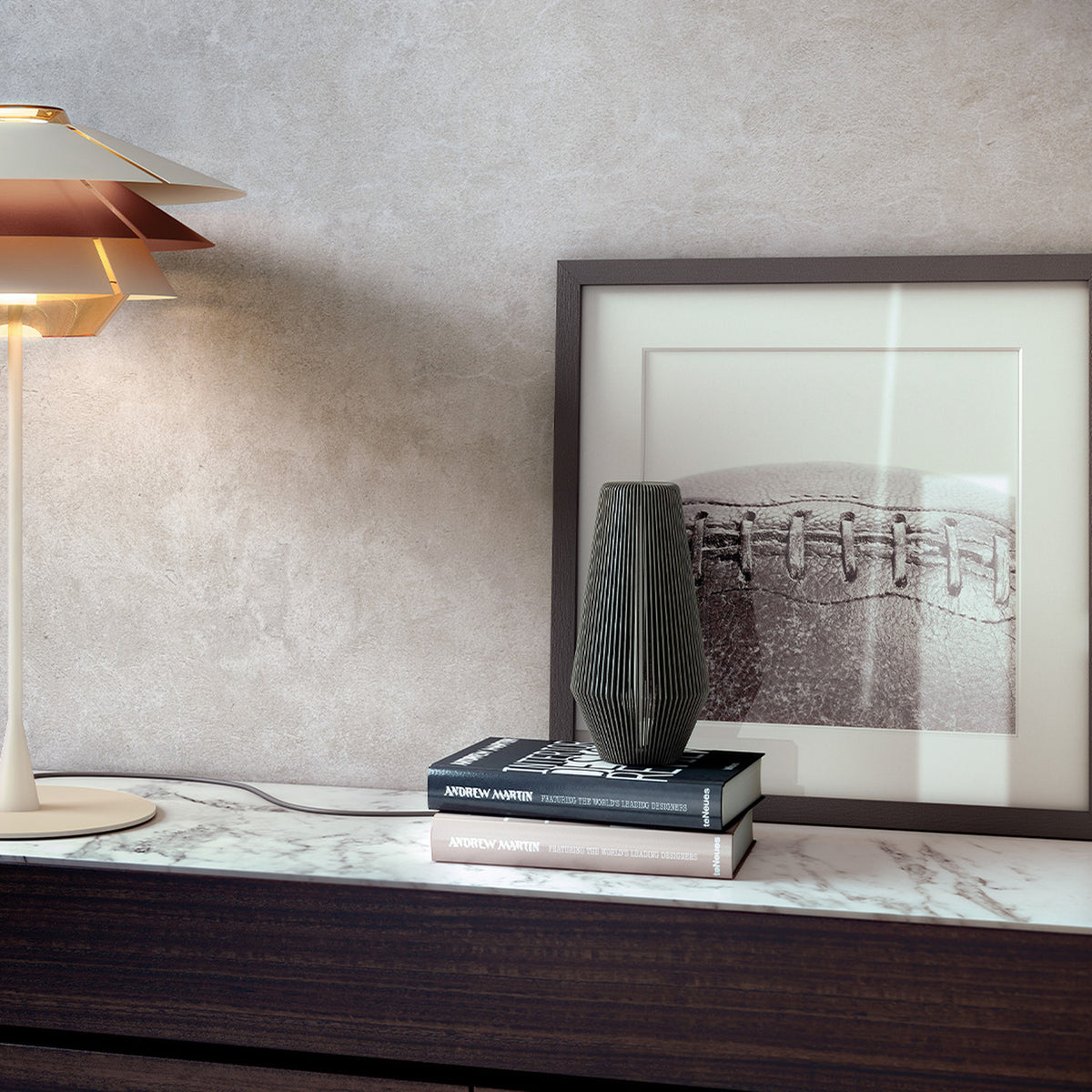 Overlay T25 Cognac Glass tiered table lamp with three stacked cone shades on a slim stem and round disc base, shown lit on a marble sideboard beside books and a framed print.