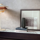 Overlay T25 Cognac Glass tiered table lamp with three stacked cone shades on a slim stem and round disc base, shown lit on a marble sideboard beside books and a framed print.