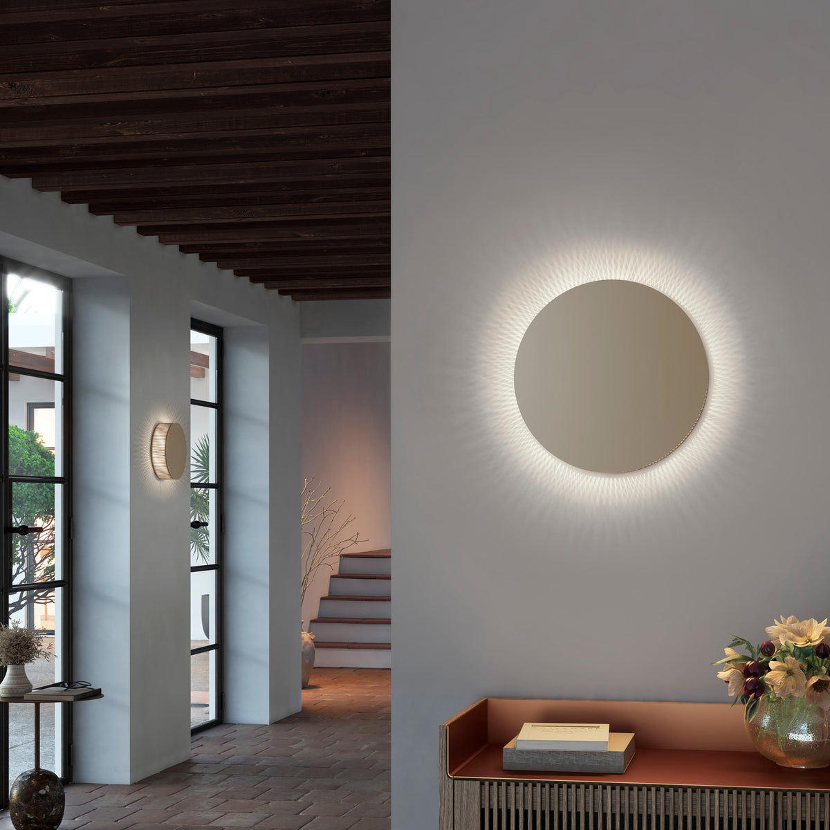 Helios A/02 round LED wall light with oak brown disc face and beige fabric thread edge, glowing warm white in a hallway and entryway setting.