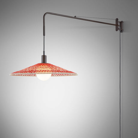 Nans 55 A/98 plug-in wall light with a long brown extending arm and wide woven cone shade in red and beige, exposed bulb beneath, shown against a plain grey background.