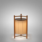 Kando P/76/R rechargeable LED floor lamp with cream pleated ribbon shade in a three-legged teak wood frame and dark round top, on a plain grey background.