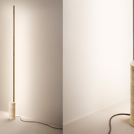 Hilow Line Travertine LED floor lamp with a slim brass-toned aluminium rod rising from a round travertine base, shown against a plain light wall.