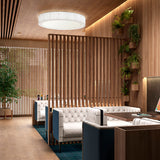 Urban PF/120 Ribbon LED ceiling light, a large round white drum fixture with ribbed fabric sides, shown lit above a wood-slatted lounge with white tufted sofas.