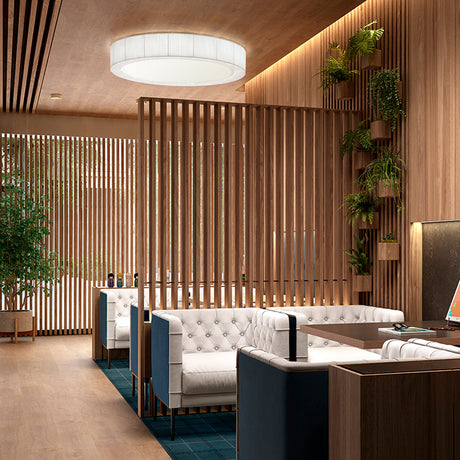 Urban PF/120 Ribbon LED ceiling light, a large round white drum fixture with ribbed fabric sides, shown lit above a wood-slatted lounge with white tufted sofas.
