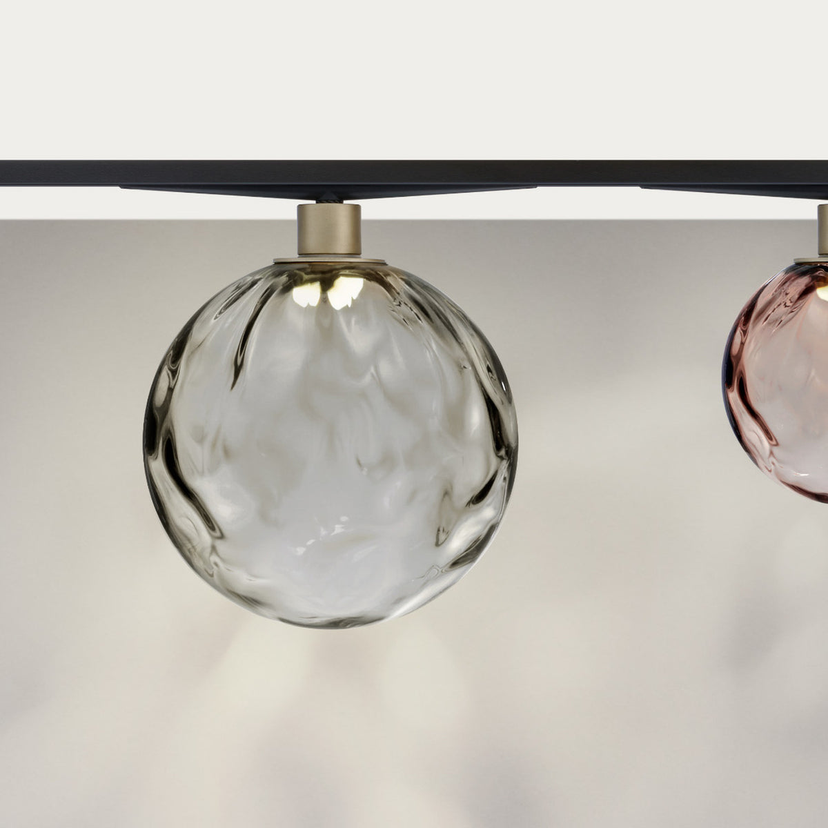 Murané Street track ceiling light with a 10cm transparent rippled glass globe on a brushed champagne collar, mounted on a black track, shown beside a pink glass globe.