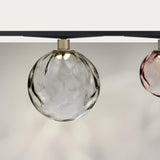 Murané Street track ceiling light with a 10cm transparent rippled glass globe on a brushed champagne collar, mounted on a black track, shown beside a pink glass globe.