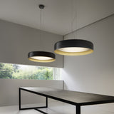 Ginevra 50 drum LED pendant lights in matt black with brass inner band, shown in pairs above a dark dining table with warm white diffused glow.