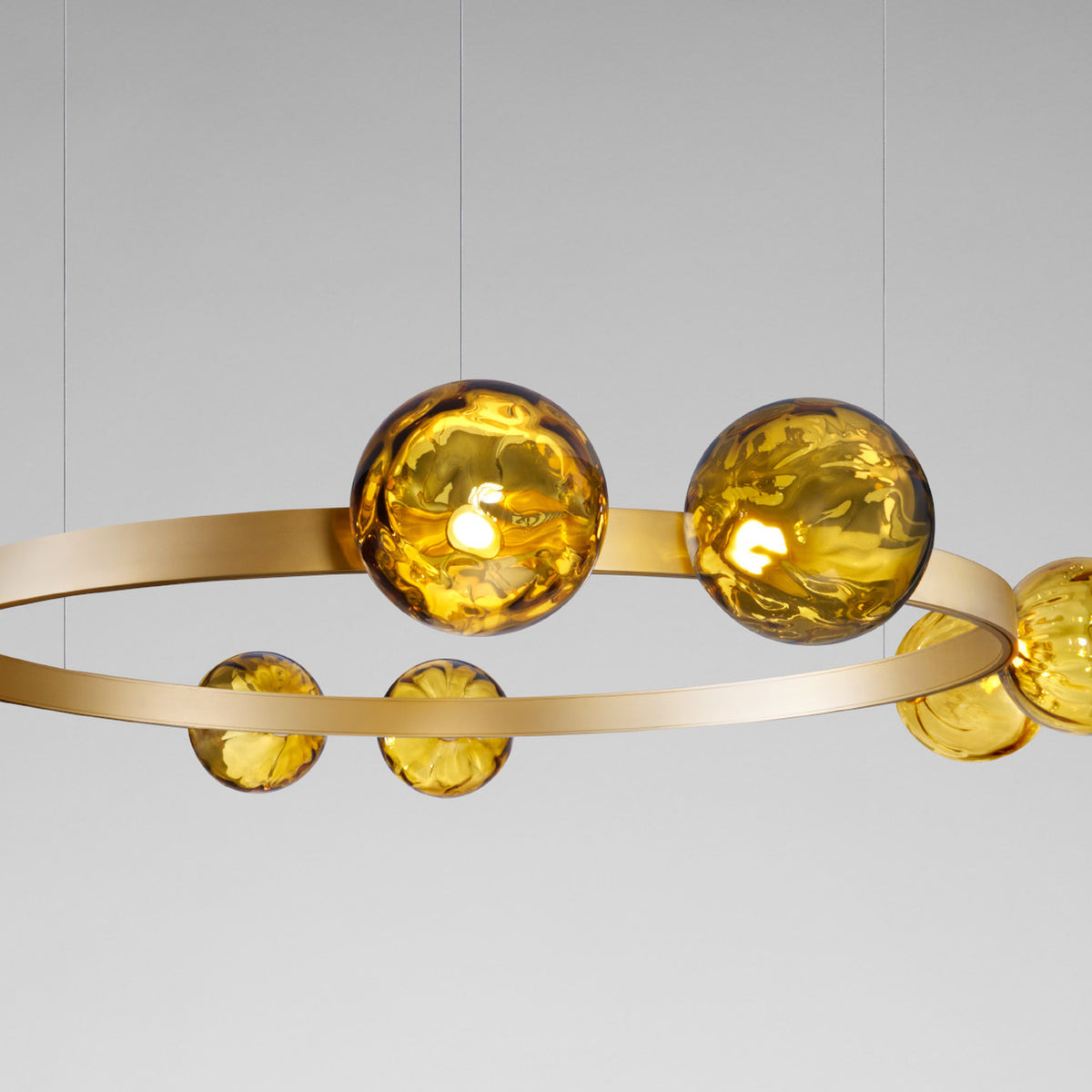 Murané R ring chandelier with brushed champagne band and caramel glass spheres of varying sizes, integrated LED, shown against a plain grey background.