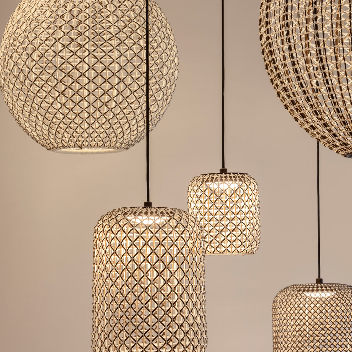 Nans S/31.2 woven outdoor pendant lights in brown, showing spherical and barrel-shaped open-lattice shades with black cables, illuminated against a neutral wall.