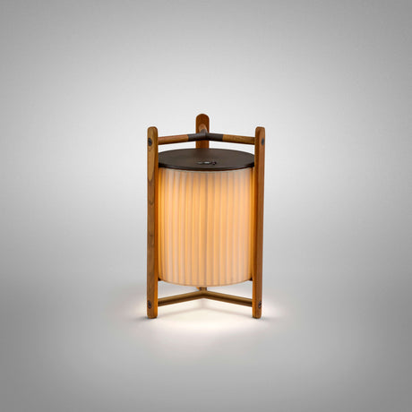 Kando M/40/R rechargeable LED table lamp with a pleated cream ribbon cylinder shade framed by teak wood posts and a dark round top disc, shown lit on a plain white background.