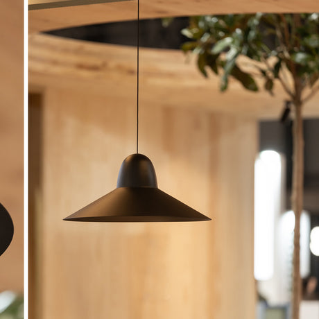 Speers SR L pendant light in black, wide shallow cone shade with rounded dome top, hung on a slim cable in a wood-panelled interior near greenery.