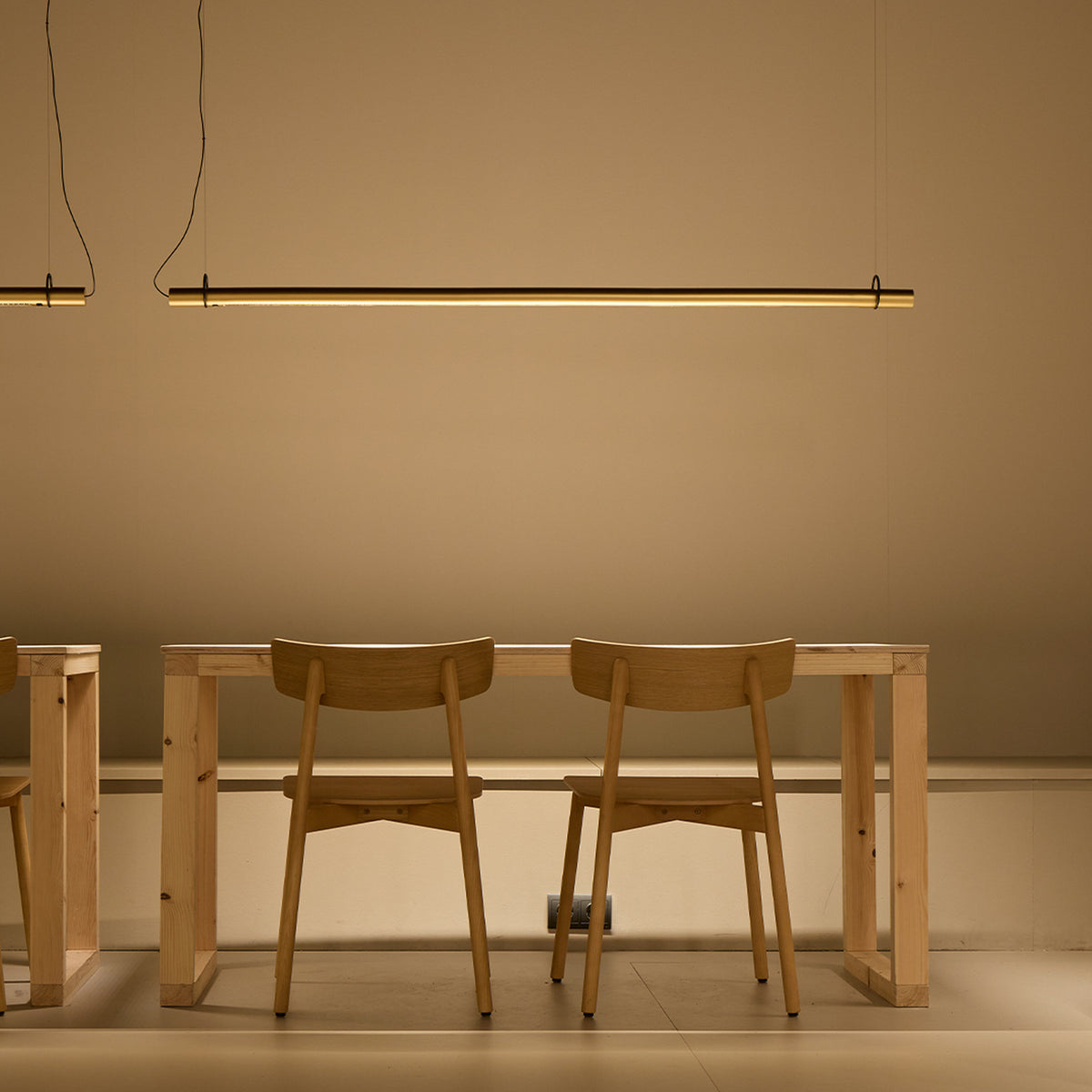 Solid SH Sens 160 cylinder LED pendant light in black finish, a slim linear tube suspended above a wooden dining table with chairs, casting warm ambient light.