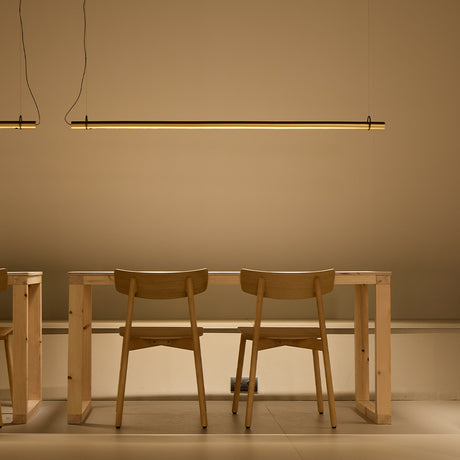 Solid SH Sens 160 cylinder LED pendant light in black finish, a slim linear tube suspended above a wooden dining table with chairs, casting warm ambient light.