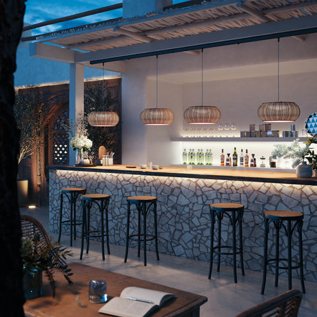 Perris S/47 Outrack woven globe pendant lights in beige hang from an outdoor pergola, illuminating a stone bar with black bar stools at dusk.