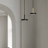 Rafaela Mono LED drum pendant in matt black, shown with a brass-stemmed pendant, both hanging in a hallway with an arched doorway.