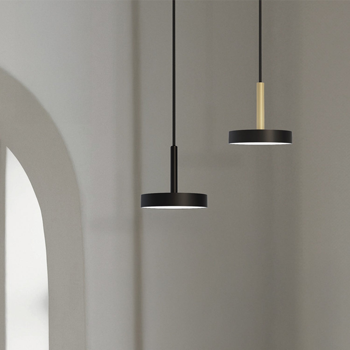 Rafaela Mono LED Drum DALI Pendant in matt black, shown with a shallow drum shade on a slim stem, alongside a similar brass-stemmed pendant against a neutral wall.