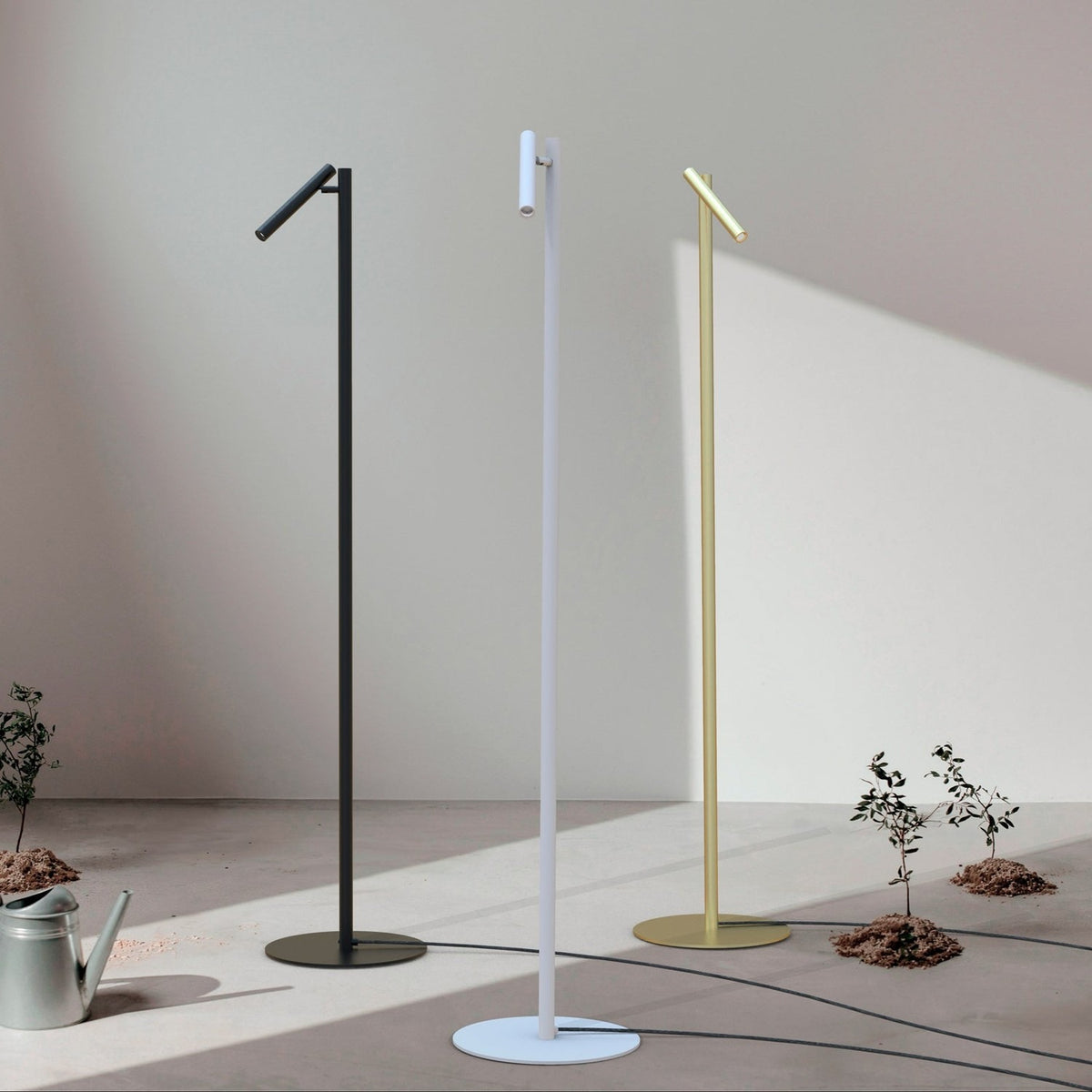 Rui LED Reading Floor Lamp in matt white, slim pole on round disc base with pivoting tubular shade, shown alongside black and brass versions in a sunlit room.