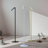 Rui LED Reading Floor Lamp in matt white, slim pole on round disc base with pivoting tubular shade, shown alongside black and brass versions in a sunlit room.
