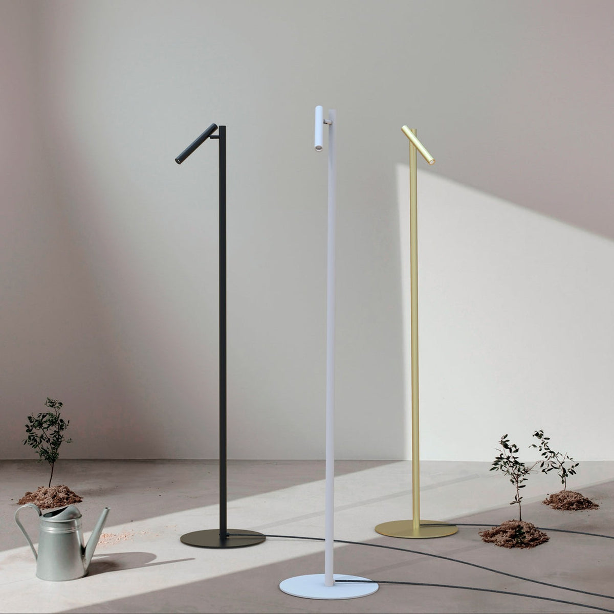 Rui LED Reading Floor Lamp in matt white, slim pole on round disc base with angled tubular shade, shown alongside black and brass versions in a sunlit room.