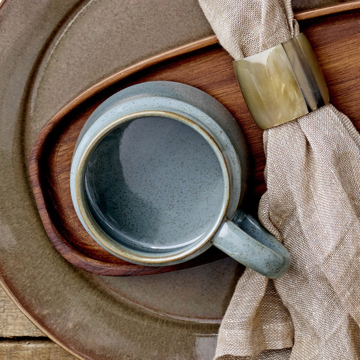 Pixie Stoneware Cup 350ml in green with a wide, low body and open loop handle, shown on a wooden tray beside a folded napkin and horn napkin ring.