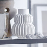 Halfdan Stoneware Vase 14cm in white, with ribbed, fluted tiers and a plain neck, displayed on a shelf beside stones and other decor pieces.