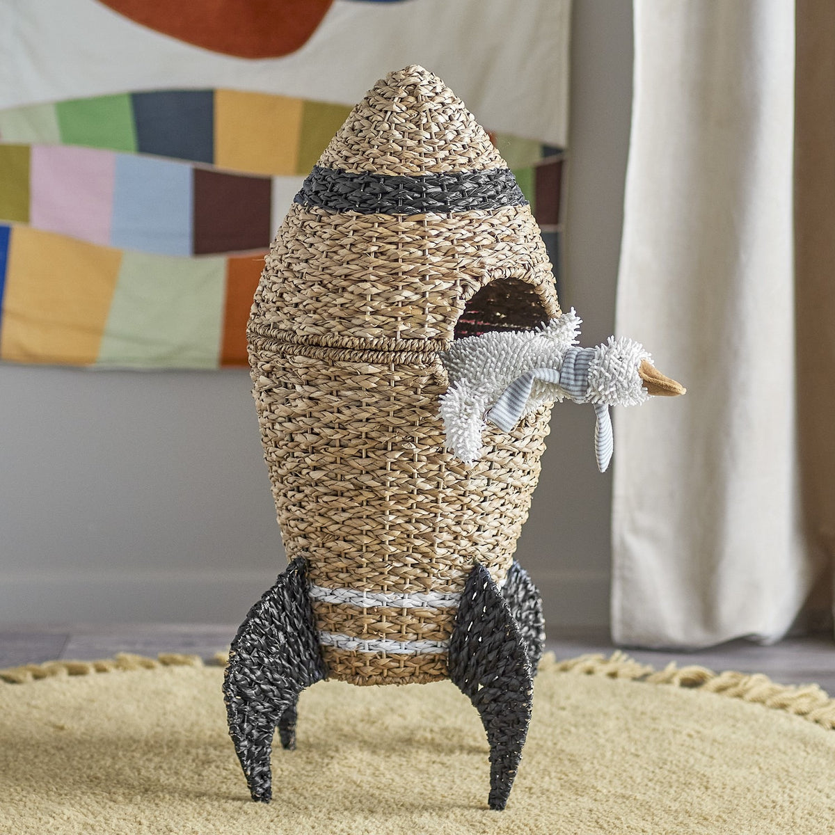 Cosmina Rocket seagrass storage basket with lid, natural woven body, dark grey fin legs and nose band, shown in a nursery with a toy duck peeking from the opening.