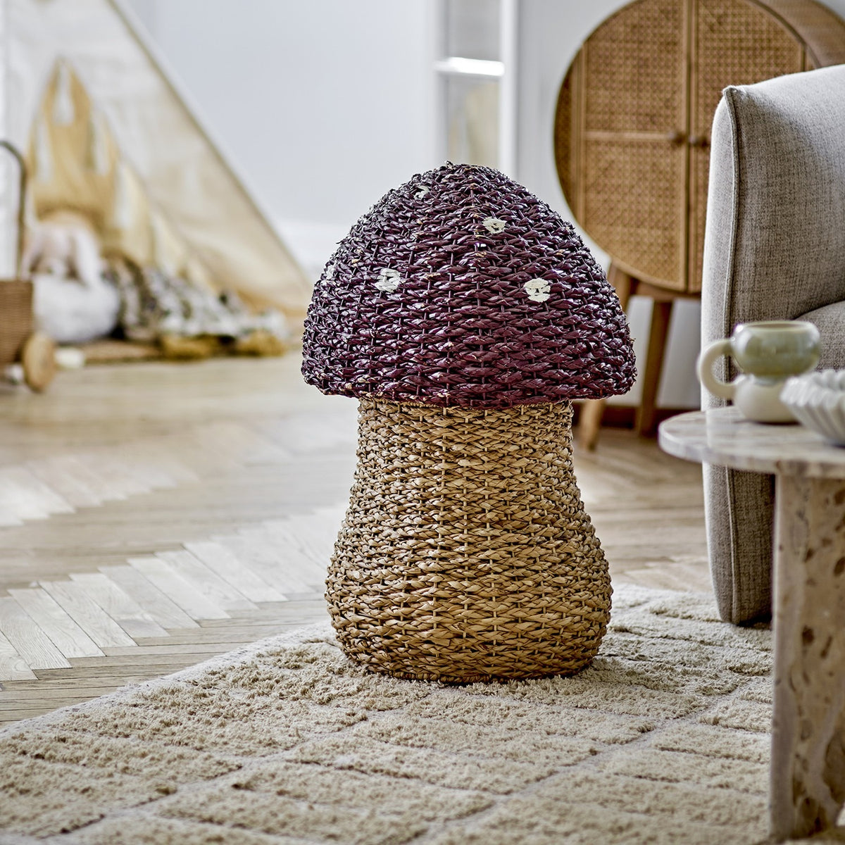 Corintha Mushroom Seagrass Basket with Lid in brown, with a woven domed cap and spotted pattern on a sturdy stem base, shown in a living room setting.