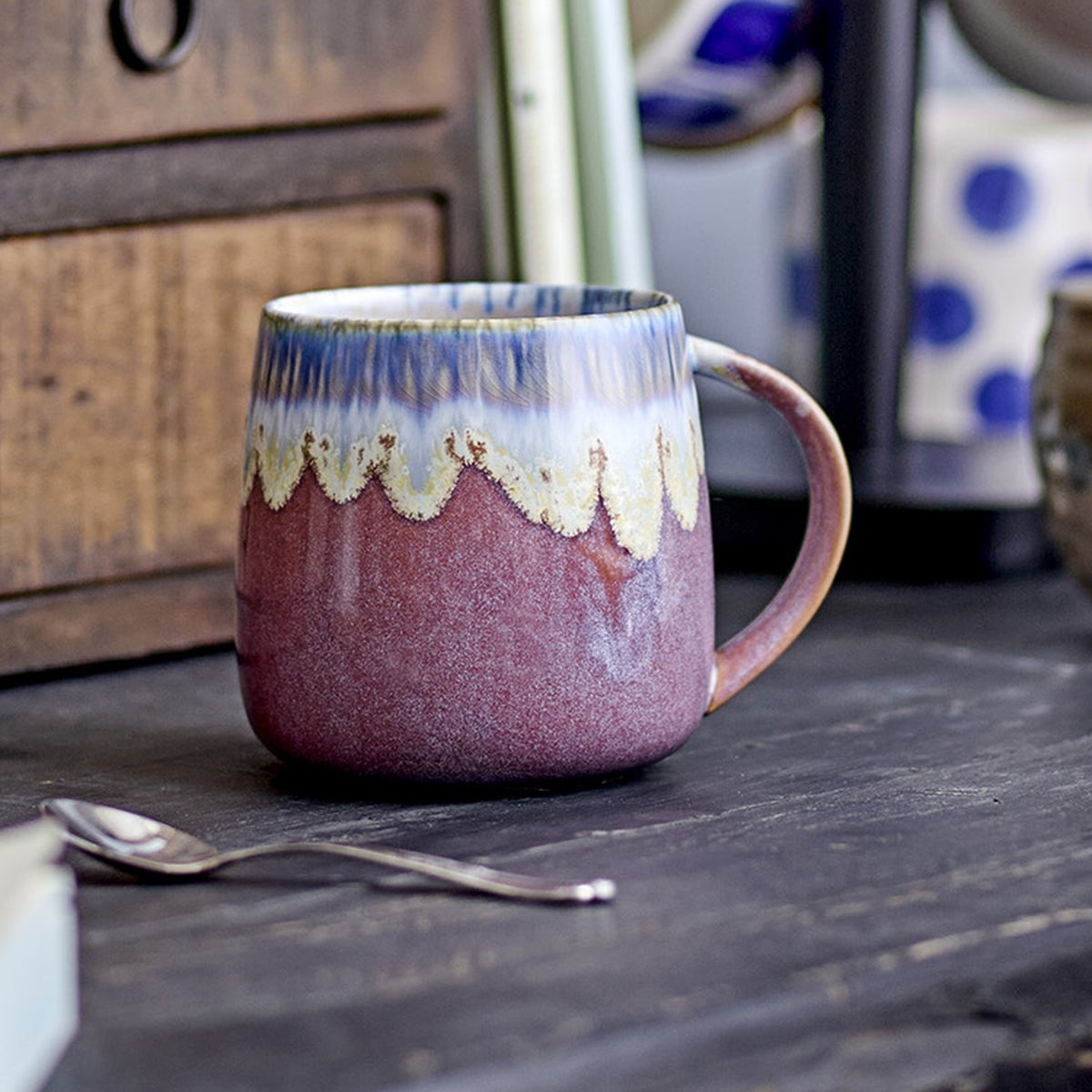 Cloe Speckled Stoneware Mug from the set of 3, pink glaze with cream drip detail fading to a blue-streaked rim, curved handle, shown on a dark wood surface.